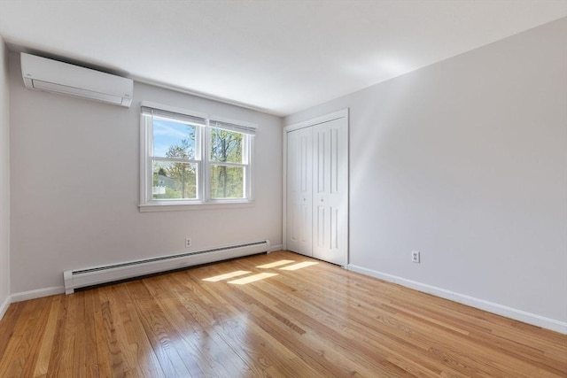 unfurnished bedroom featuring baseboards, a wall unit AC, wood finished floors, a baseboard radiator, and a closet