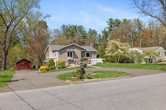 ranch-style house with an outdoor structure, a front lawn, curved driveway, a shed, and a chimney