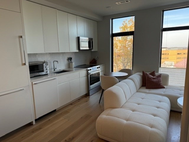 kitchen with light hardwood / wood-style floors, white cabinets, stainless steel appliances, and backsplash