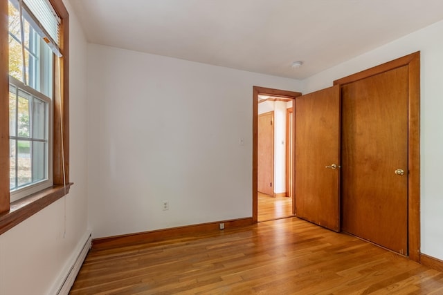 unfurnished bedroom with a baseboard radiator and light hardwood / wood-style floors