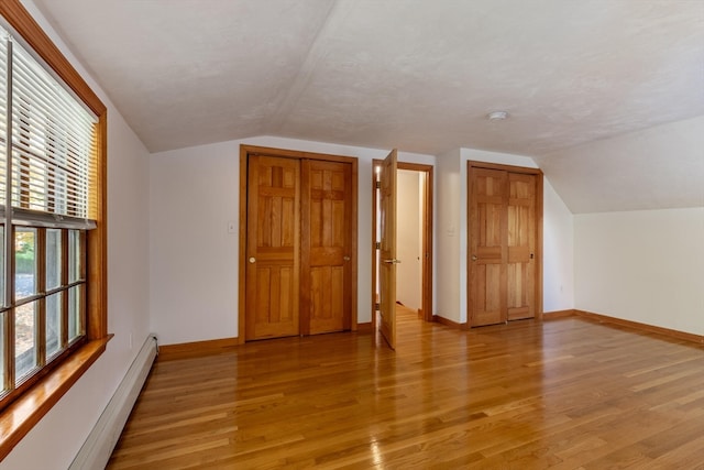 additional living space featuring lofted ceiling, light hardwood / wood-style floors, and a baseboard radiator