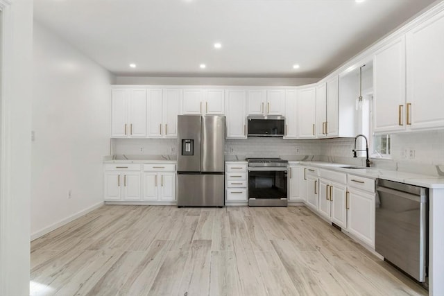 kitchen with a sink, light wood-type flooring, white cabinetry, decorative backsplash, and appliances with stainless steel finishes