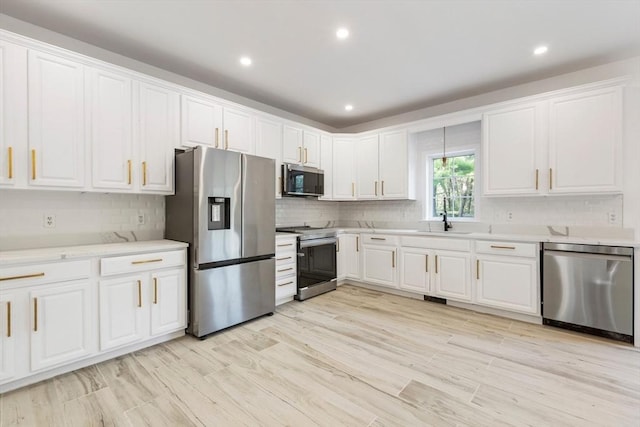 kitchen with a sink, white cabinetry, backsplash, light countertops, and appliances with stainless steel finishes