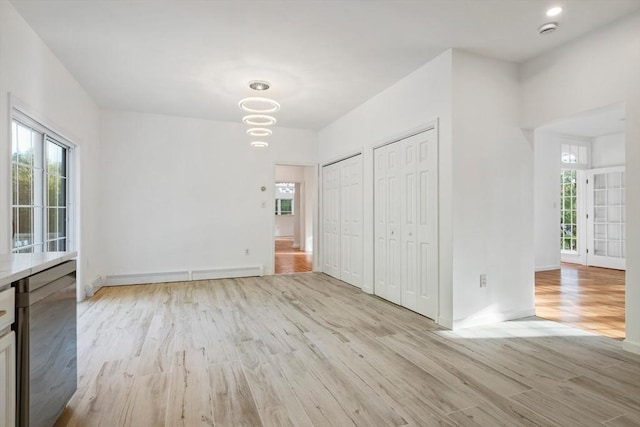 unfurnished bedroom with a baseboard heating unit, baseboards, multiple closets, and light wood-style floors
