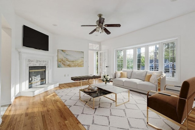 living area featuring baseboards, a fireplace, ceiling fan, and wood finished floors