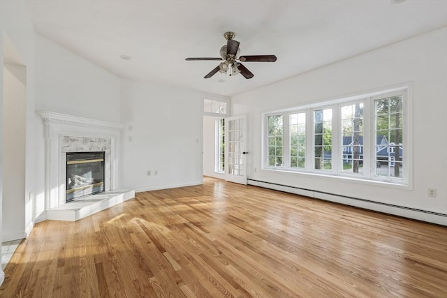 unfurnished living room featuring a high end fireplace, a baseboard heating unit, light wood-type flooring, a ceiling fan, and baseboards