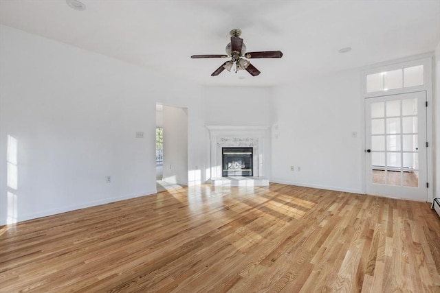 unfurnished living room with a premium fireplace, light wood finished floors, baseboards, and ceiling fan
