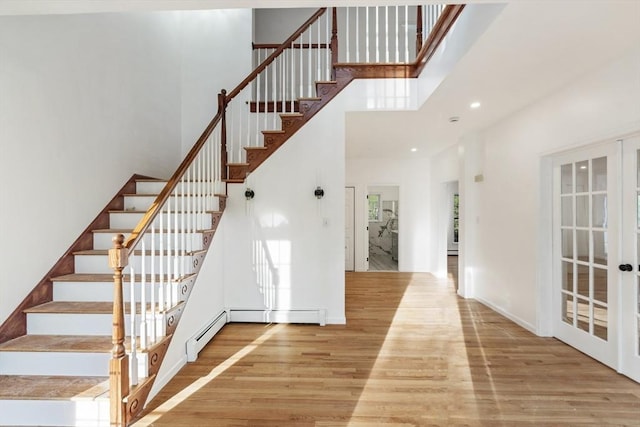 staircase featuring french doors, a baseboard heating unit, wood finished floors, recessed lighting, and a high ceiling