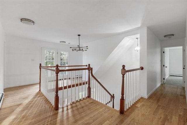 stairway featuring a baseboard heating unit, wood finished floors, an inviting chandelier, a baseboard radiator, and baseboards