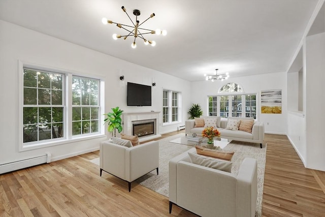 living room featuring a glass covered fireplace, a baseboard radiator, an inviting chandelier, and light wood-style flooring