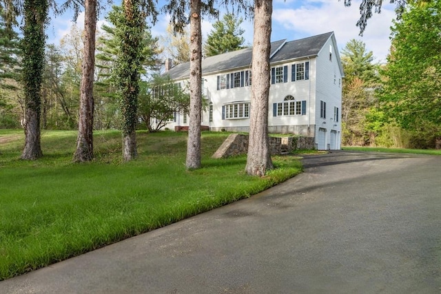 colonial-style house featuring driveway, a chimney, and a front yard