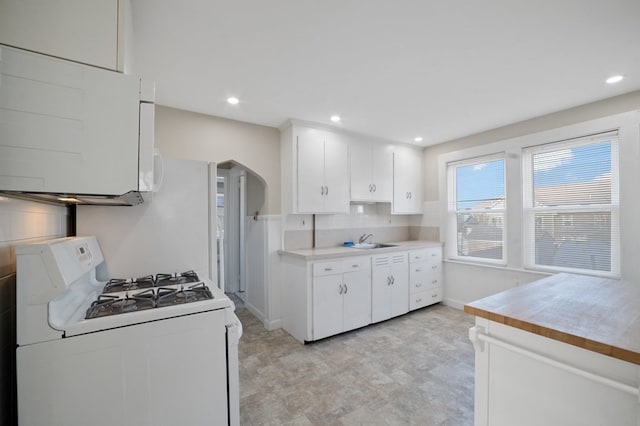 kitchen with decorative backsplash, white cabinets, white gas range oven, and sink