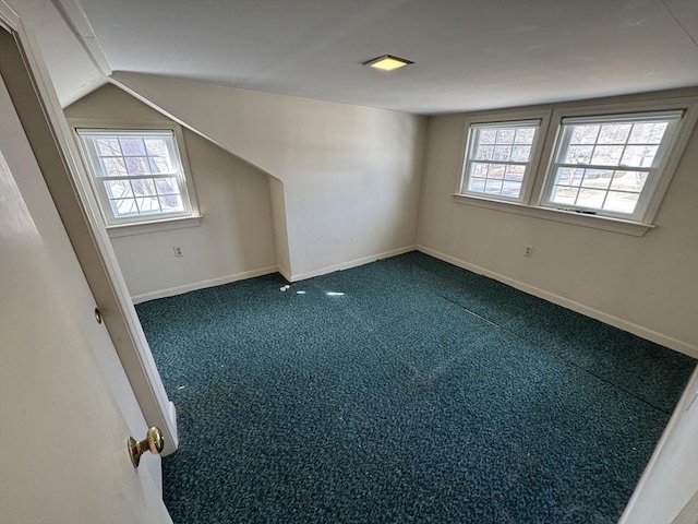 additional living space featuring baseboards, lofted ceiling, and dark colored carpet