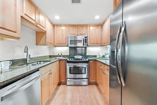 kitchen featuring light brown cabinetry, sink, light wood-type flooring, dark stone countertops, and appliances with stainless steel finishes