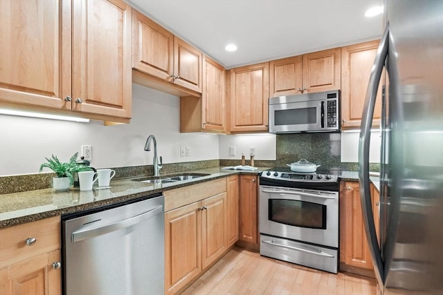 kitchen featuring stainless steel appliances, sink, dark stone countertops, and light wood-type flooring