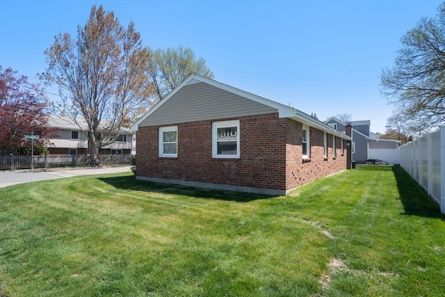 view of side of home featuring a lawn, brick siding, and fence