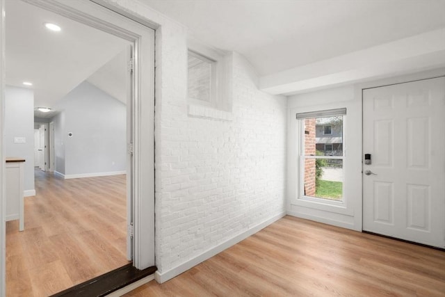 doorway with light wood-style floors, lofted ceiling, and brick wall