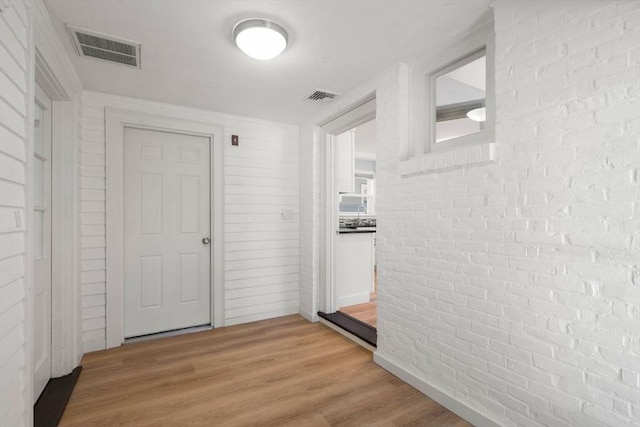 interior space with light wood-type flooring, brick wall, and visible vents