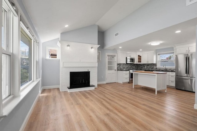 kitchen with vaulted ceiling, a sink, open floor plan, stainless steel appliances, and white cabinetry