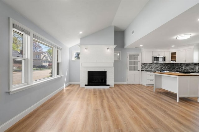 unfurnished living room with recessed lighting, vaulted ceiling, light wood-style flooring, and a fireplace