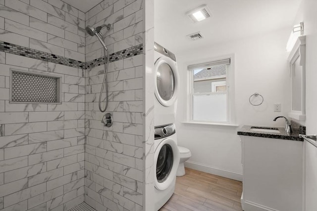 full bath featuring toilet, visible vents, tiled shower, and stacked washer and clothes dryer