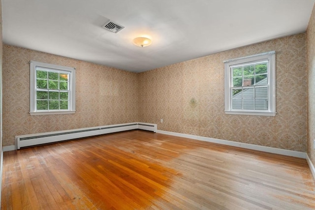 unfurnished room featuring a healthy amount of sunlight, a baseboard radiator, and light hardwood / wood-style floors