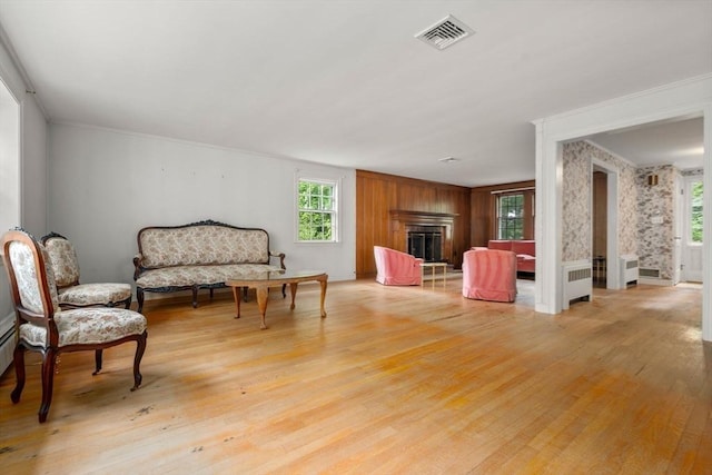 living area with a fireplace, radiator heating unit, light hardwood / wood-style floors, and ornamental molding