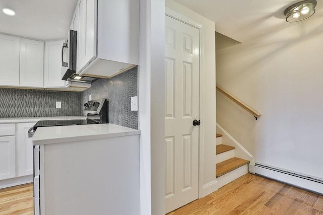 kitchen featuring white cabinets, light wood-type flooring, baseboard heating, and backsplash