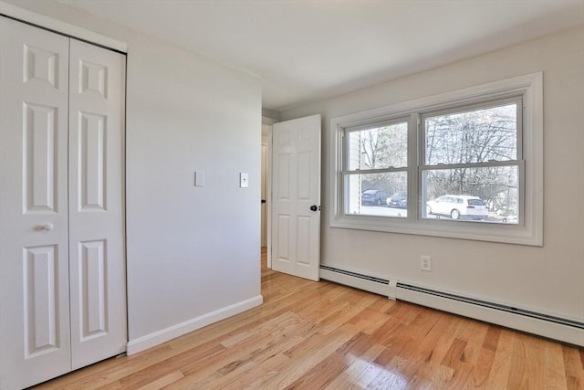 unfurnished bedroom featuring a closet, light wood-type flooring, and a baseboard heating unit