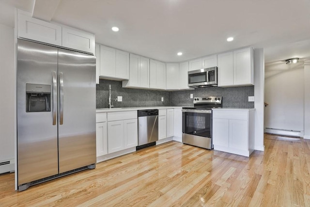 kitchen featuring decorative backsplash, stainless steel appliances, baseboard heating, light hardwood / wood-style flooring, and white cabinetry