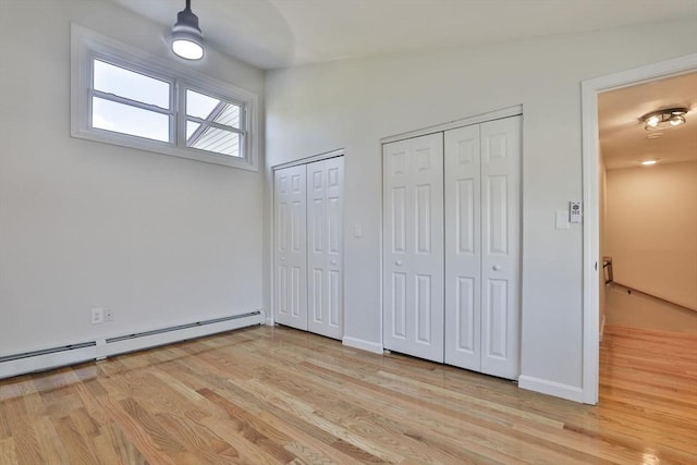 unfurnished bedroom with vaulted ceiling, ceiling fan, a baseboard heating unit, light hardwood / wood-style flooring, and multiple closets