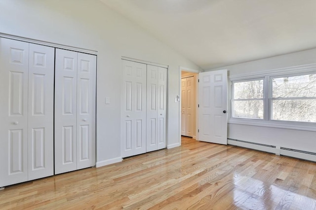 unfurnished bedroom featuring a baseboard heating unit, vaulted ceiling, light hardwood / wood-style flooring, and multiple closets