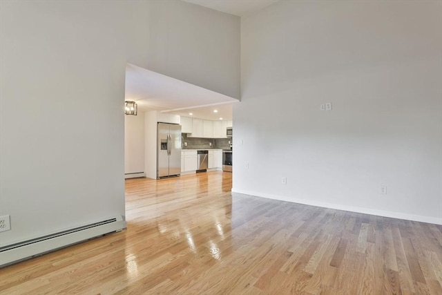 unfurnished living room featuring baseboard heating, light hardwood / wood-style flooring, and a towering ceiling