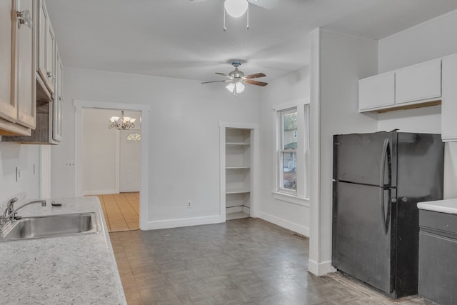 kitchen with black fridge, sink, ceiling fan with notable chandelier, and white cabinets