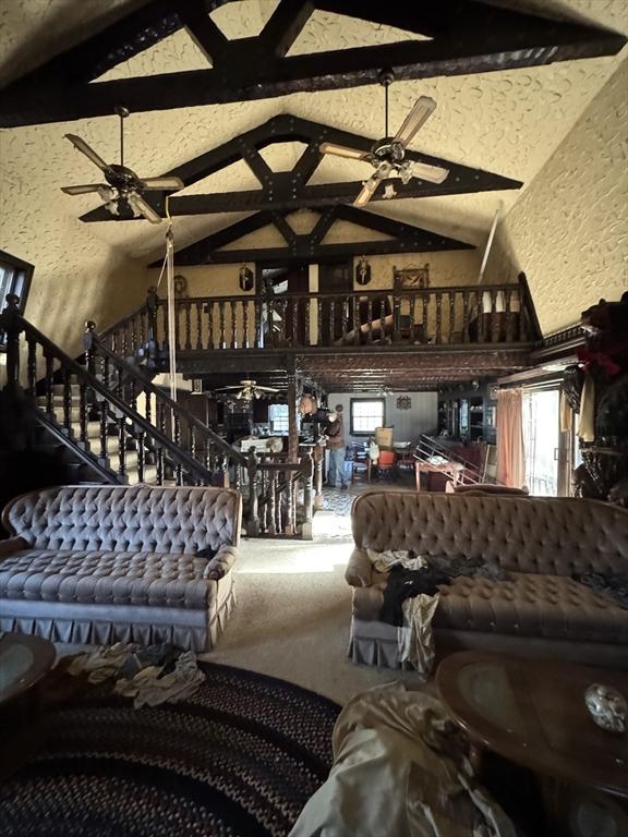 living room with a ceiling fan, vaulted ceiling with beams, and a textured wall