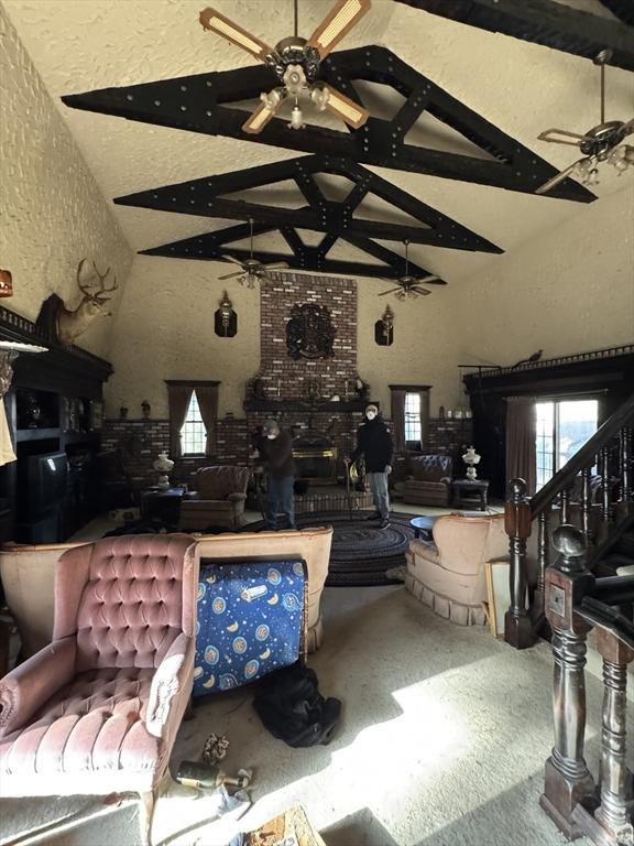 living area with beam ceiling, high vaulted ceiling, ceiling fan, and a textured wall