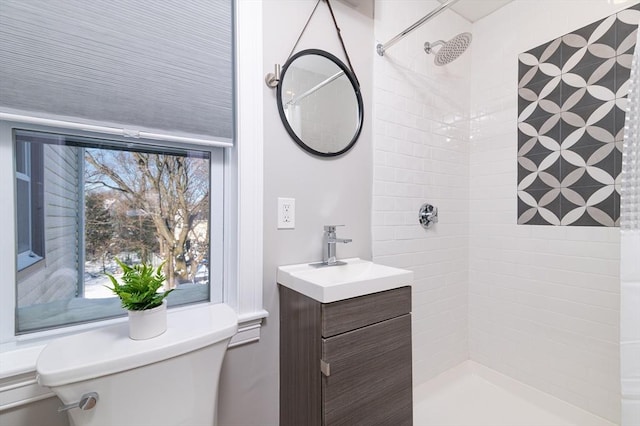 bathroom with toilet, tiled shower, and vanity