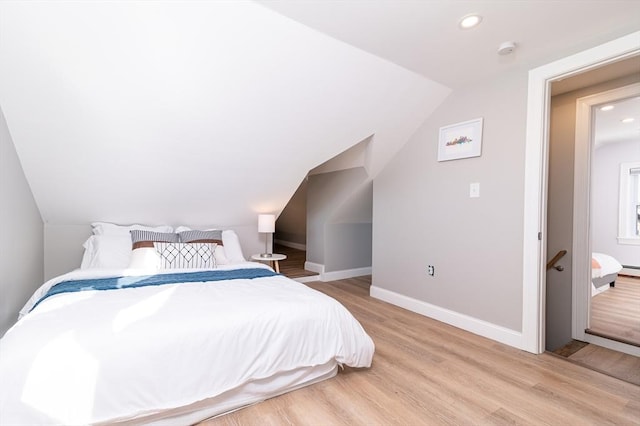 bedroom with lofted ceiling, a baseboard radiator, and light hardwood / wood-style flooring