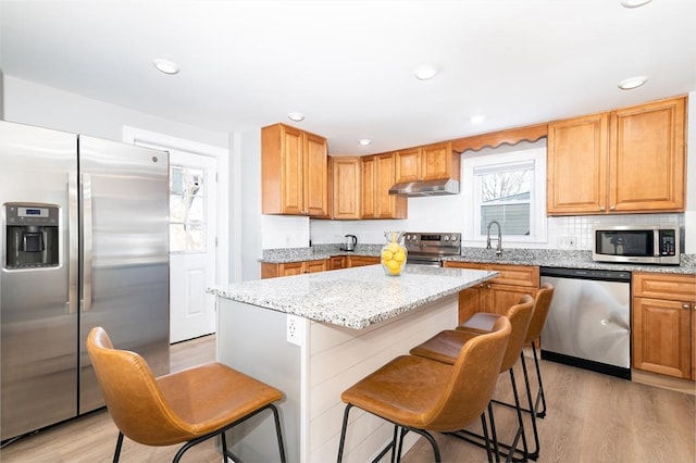 kitchen featuring a kitchen island, stainless steel appliances, light wood-type flooring, and light stone counters