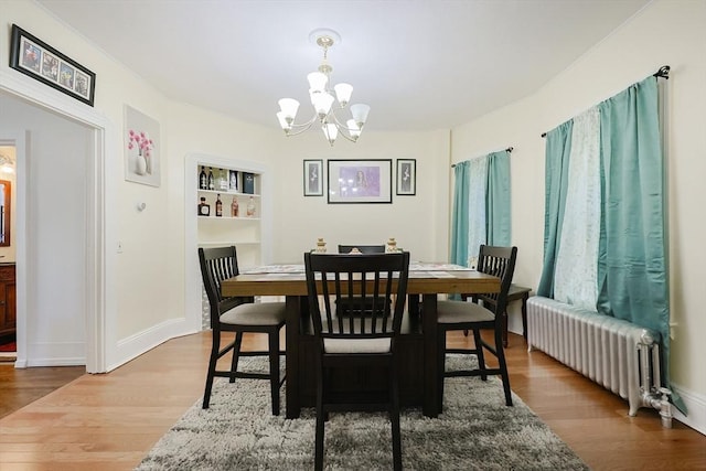 dining area with a chandelier, radiator, baseboards, and wood finished floors