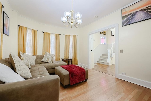 living area featuring a notable chandelier, light wood finished floors, stairway, ornamental molding, and baseboards