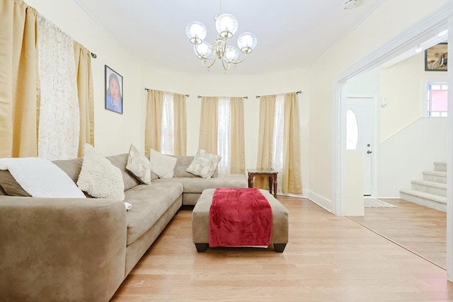 living area featuring light wood finished floors, baseboards, ornamental molding, an inviting chandelier, and stairs