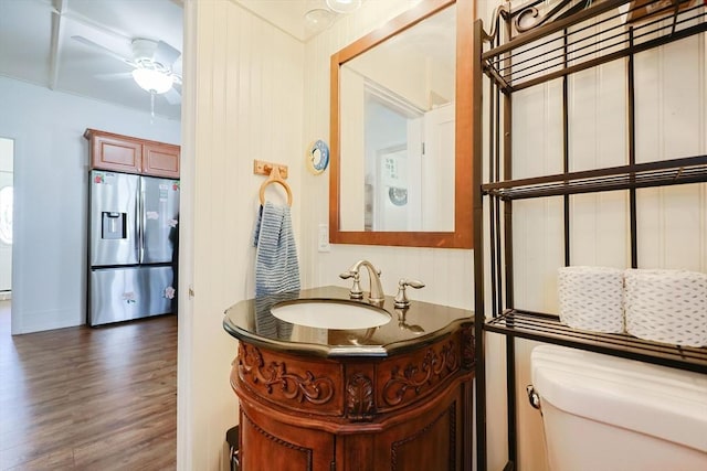 half bath with a ceiling fan, vanity, toilet, and wood finished floors