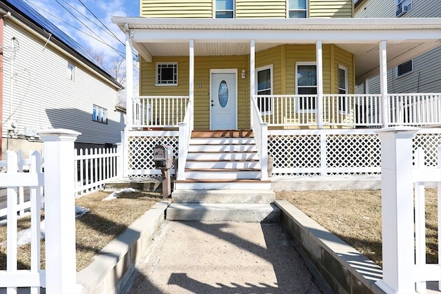 view of exterior entry with covered porch and fence