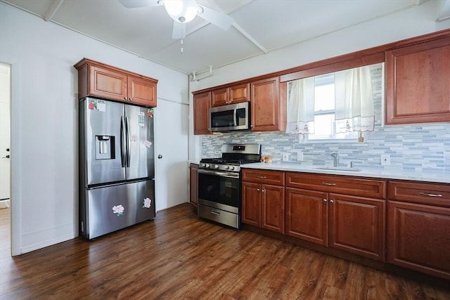 kitchen featuring brown cabinets, dark wood-type flooring, a sink, stainless steel appliances, and backsplash