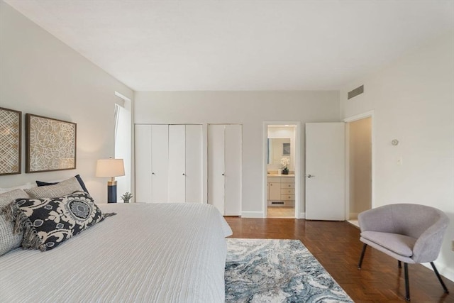 bedroom with baseboards, two closets, ensuite bath, and visible vents