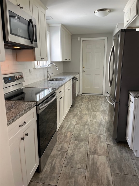 kitchen featuring white cabinets, sink, decorative backsplash, dark stone countertops, and appliances with stainless steel finishes