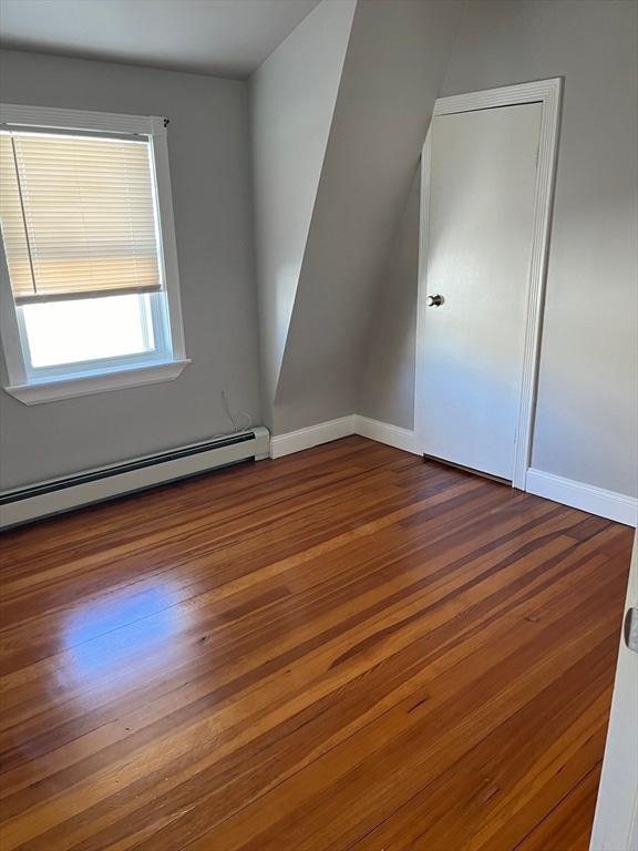 empty room with dark hardwood / wood-style flooring and a baseboard radiator