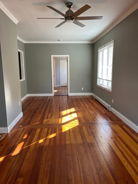 empty room featuring dark hardwood / wood-style floors, baseboard heating, crown molding, and ceiling fan