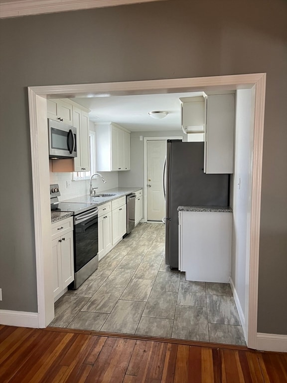 kitchen featuring appliances with stainless steel finishes, light wood-type flooring, light stone counters, sink, and white cabinets